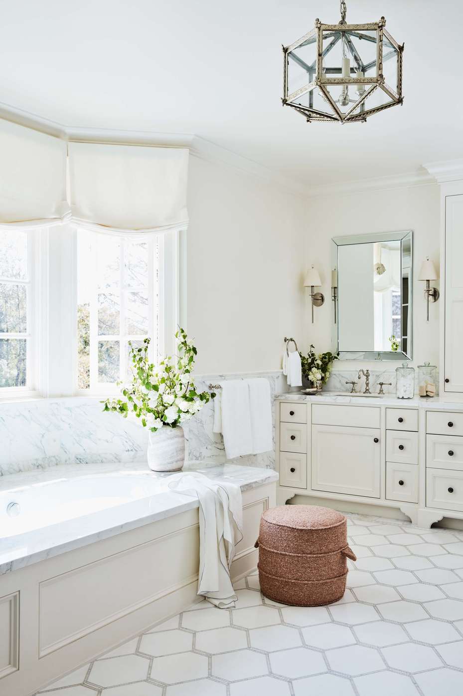 Geometric white bathroom design ideas showcasing a white tub over small white hexagon floor tiles with dark grout.