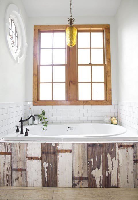 Rustic white bathroom design ideas featuring a freestanding tub placed beside a reclaimed natural wood window frame.