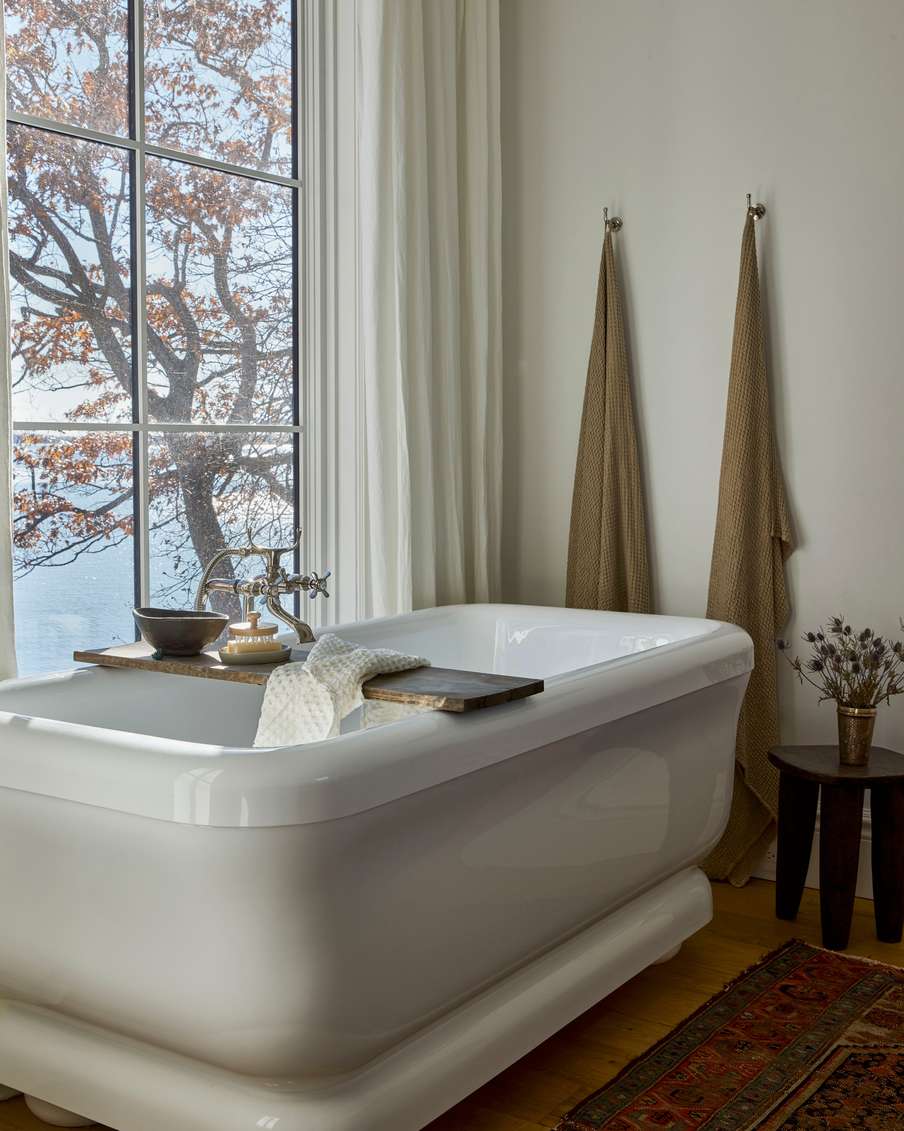 Bright white bathroom design ideas highlighting a white soaking tub positioned in front of a floor-to-ceiling view window.