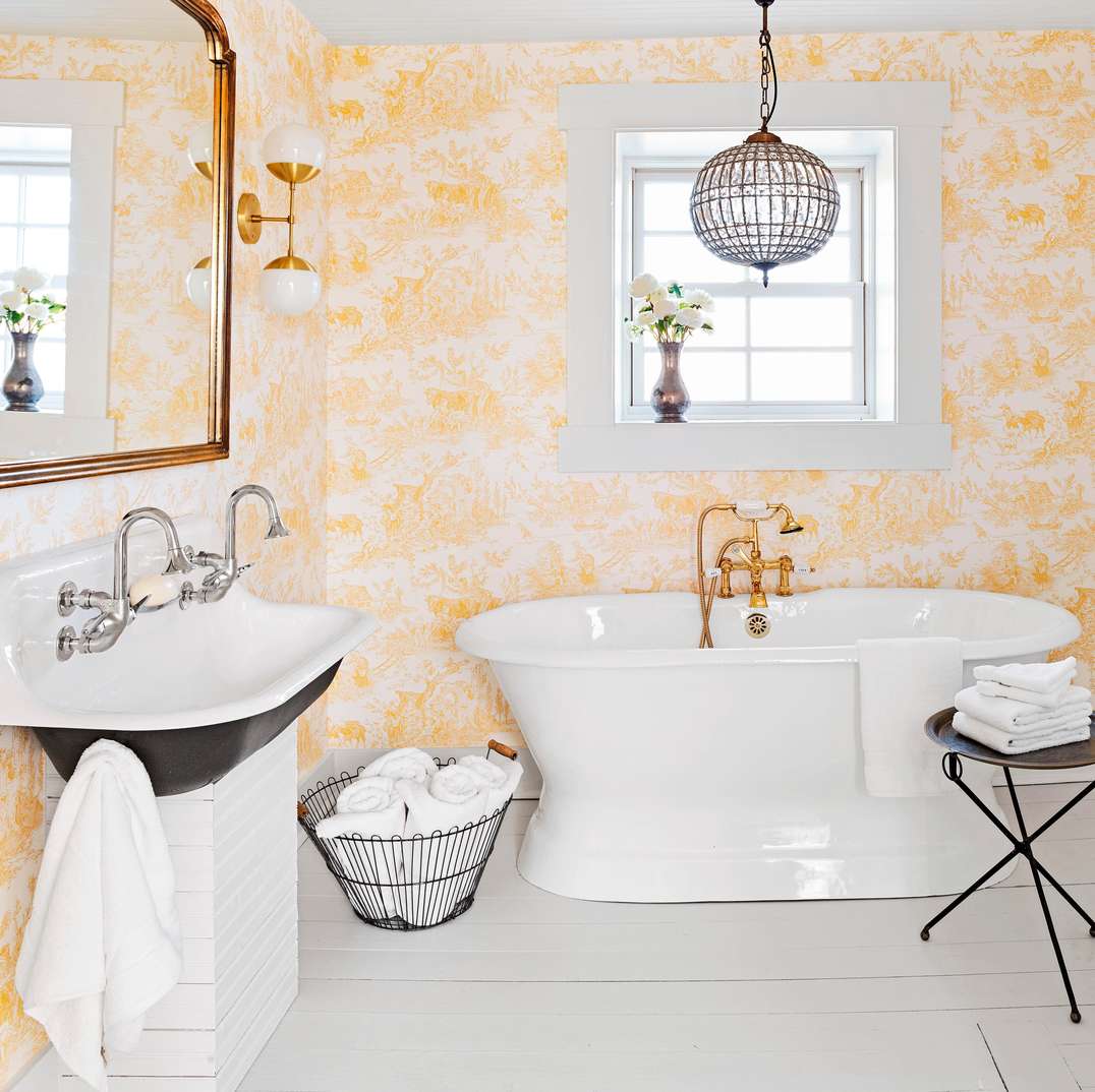 Vibrant white bathroom design ideas displaying a white clawfoot tub set against cheerful yellow botanical wallpaper.