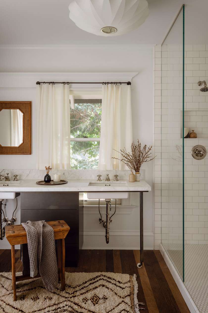 Scandinavian white bathroom design ideas featuring a white marble vanity accented by a rustic wooden stool.