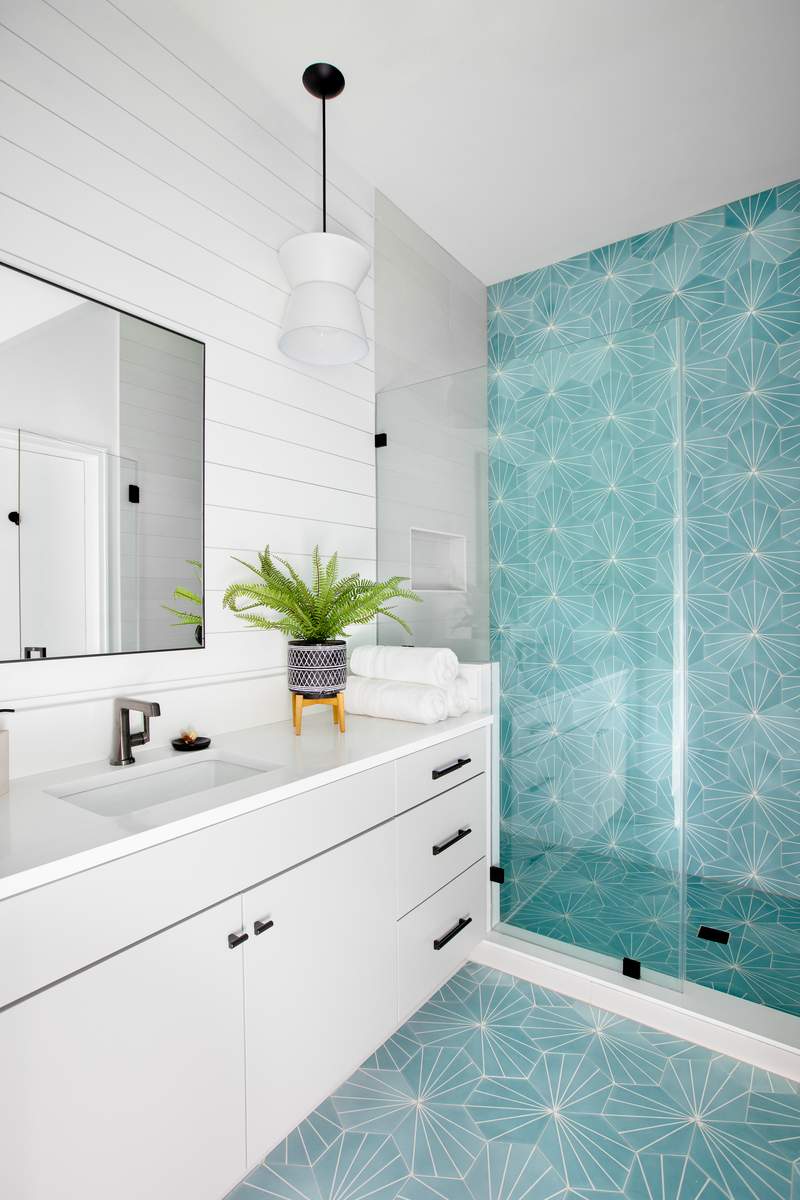 Walk-in shower featuring glossy teal tile set against white bathroom walls and matte black fixtures.