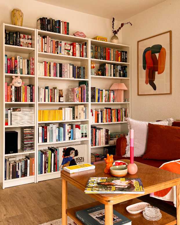 White freestanding bookcase, vibrant patterned armchair, teal rug, natural light, pastel accents.