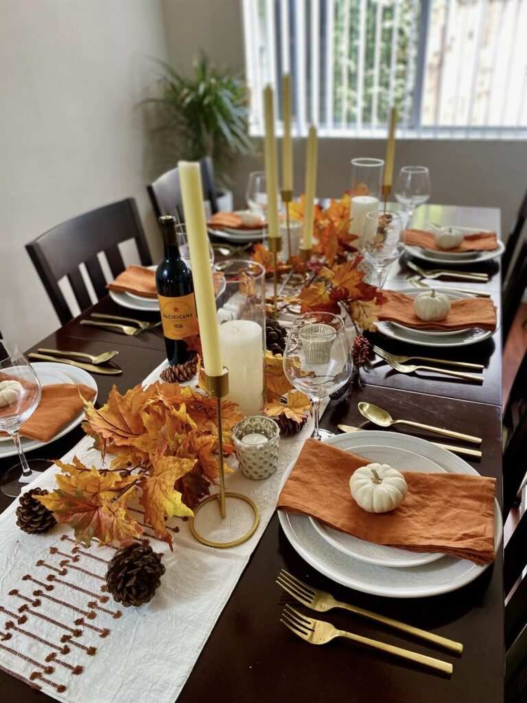 Dining table with white pumpkins, terracotta plates, muted green foliage, warm candlelight, balanced color scheme