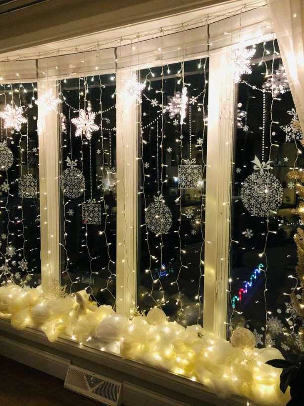 Large living‑room window with sheer curtains, threaded with warm white fairy lights that cascade down the fabric.