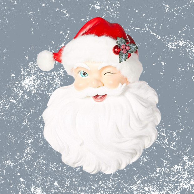 Framed winking santa face wall art in a red frame on a white wall with a small plant.