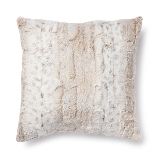 Plush neutral faux fur pillow styled on textured wool sofa with soft ambient background lighting