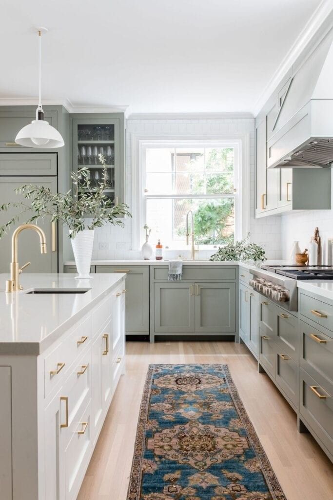 Warm kitchen interior featuring deep forest green runner rug wood cabinets counter foliage and warm pendant light