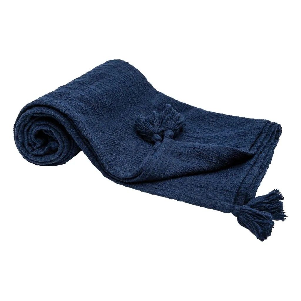 Camel leather armchair draped with deep navy blue chunky knit throw pillow and warm ambient lighting