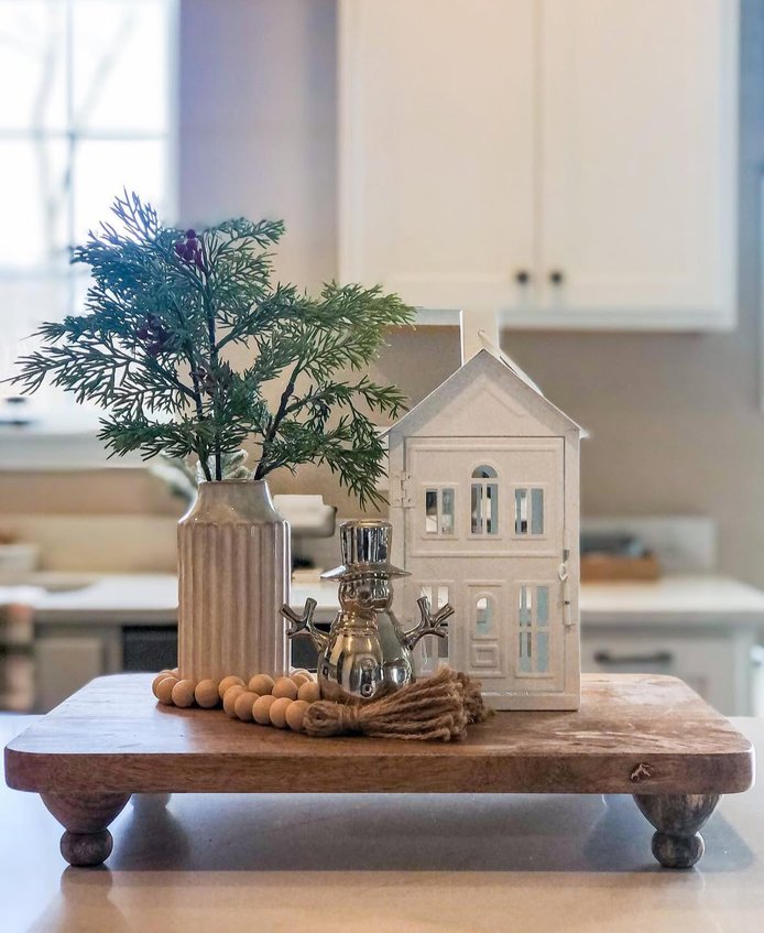 Glass lantern with a small house inside and a candle, placed on a kitchen shelf.