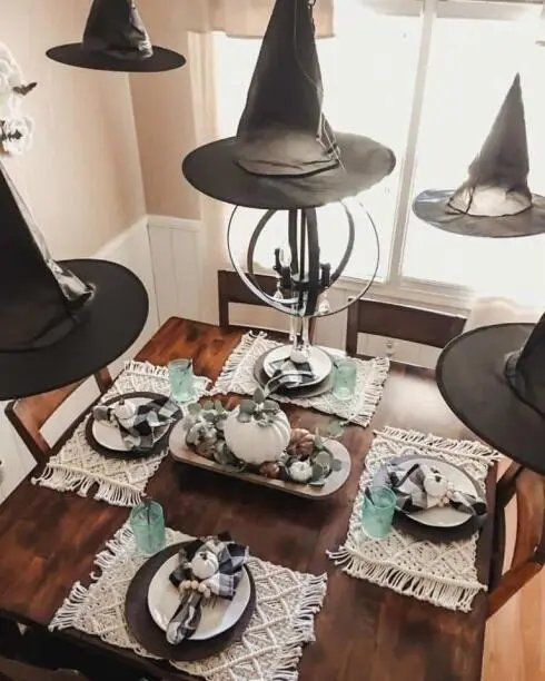 Dining table with hanging witch hats, macrame plant hangers, and warm string lights.