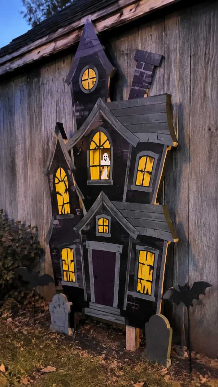 Large wooden haunted house cutout with glowing windows in the yard.