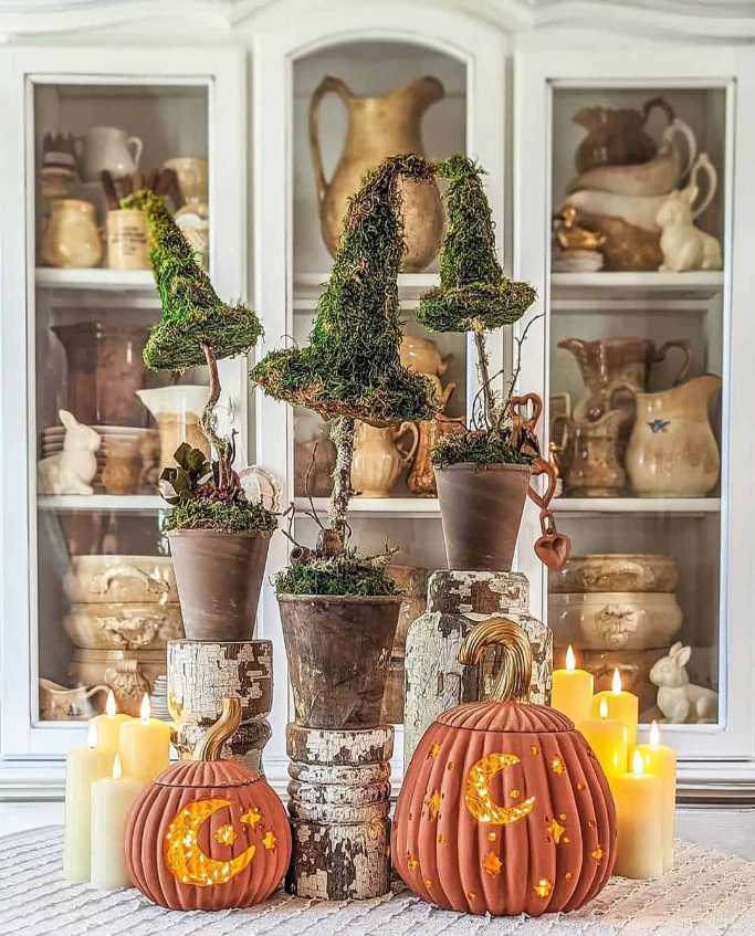 Witch hat on a moss-covered topiary stand with carved moon pumpkins.