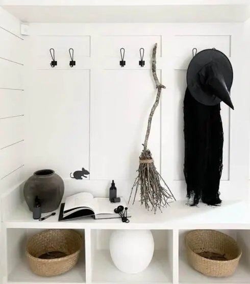 Mudroom bench with a twig broom and black cloak hanging nearby.