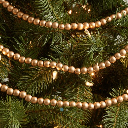 Natural wood bead garland wrapped around a small tree with greenery and lights.