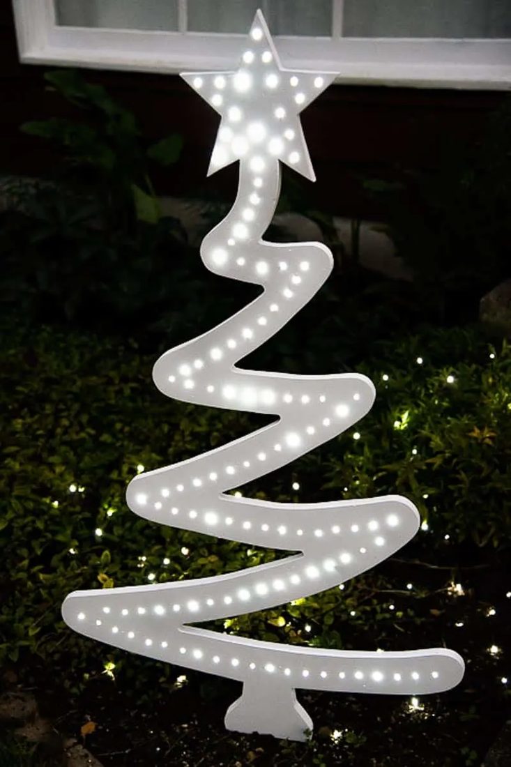 A modern, triangular wooden tree frame illuminated with lights as outdoor christmas decorations.
